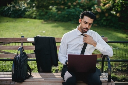 A man with a white shirt and a tie sitting on a bench researching careers with an MS in Global Risk